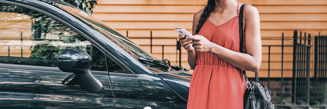 Woman booking Rhode Island car service on phone next to luxury vehicle