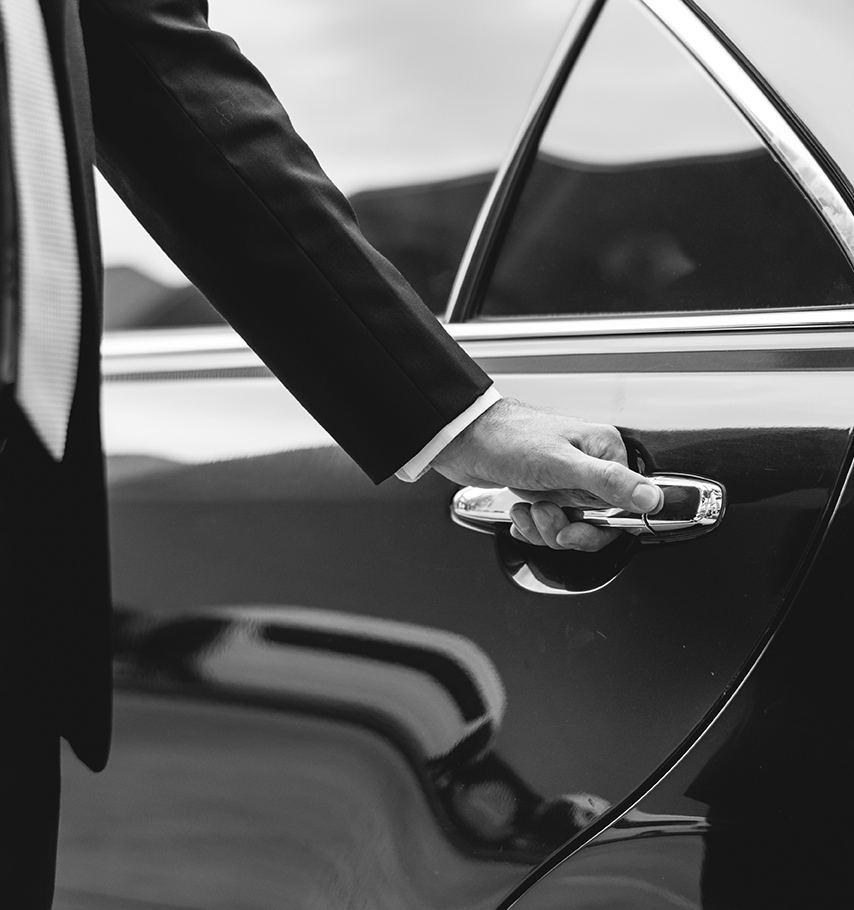 Professional chauffeur opening car door for luxury transportation client